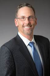 A person wearing a suit and tie smiling at the camera  Description generated with very high confidence